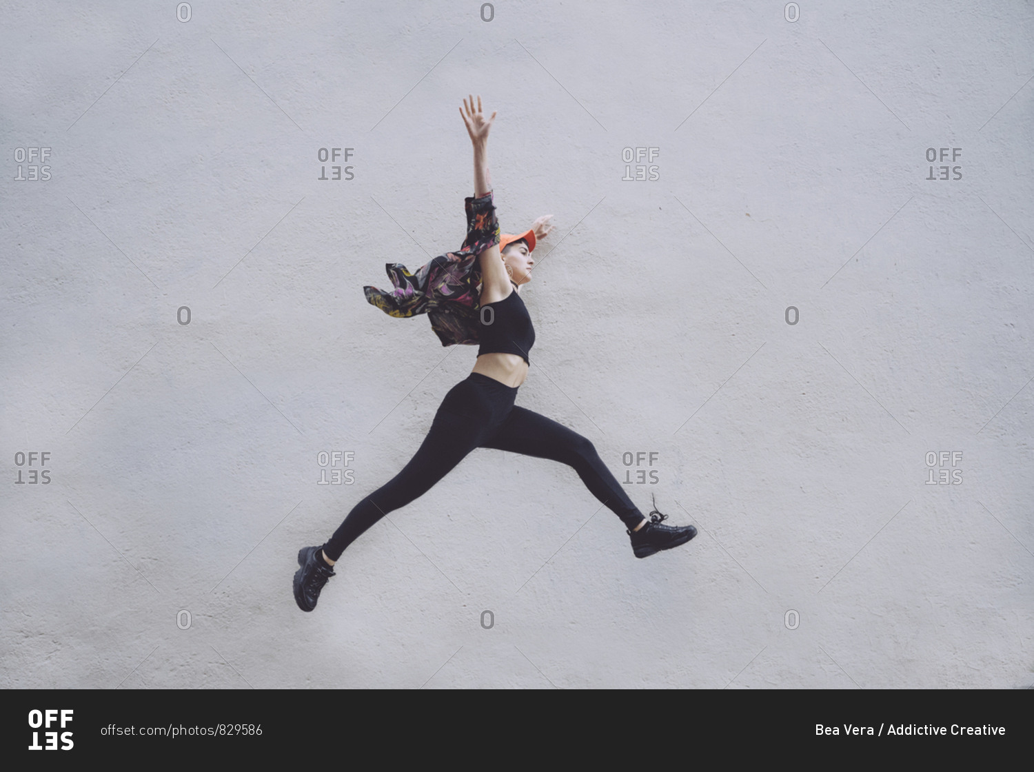 Side view of young sportive woman in black leggings with legs spread wide along wall