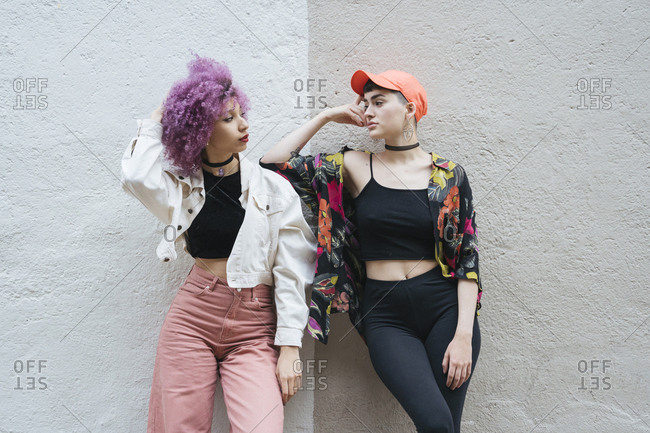 Girlfriends leaning on wall posing side by side together and looking at each other