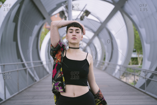 Young brunette woman in colorful shirt and black clothes posing in round tunnel and looking at camera