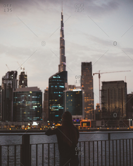 Back view of person standing on embankment against glowing skyscrapers of Dubai city
