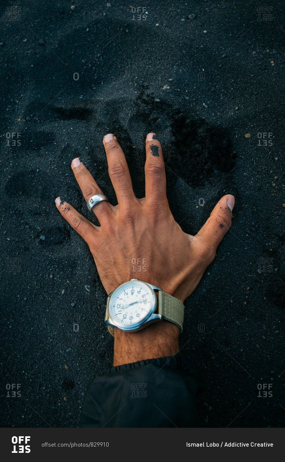 From above hand of anonymous man with ring and watch touching black dirt in countryside