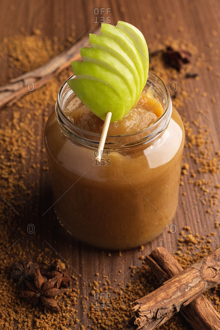 Decorated with green apple appetizing juicy applesauce in glass jar and cinnamon on wooden background