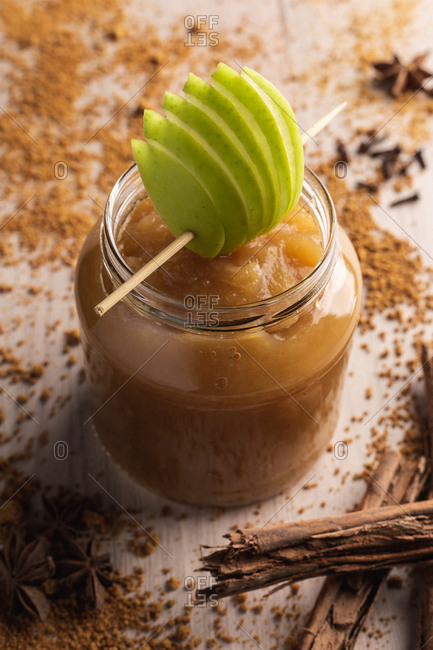 Decorated with green apple appetizing juicy applesauce in glass jar and cinnamon on wooden background