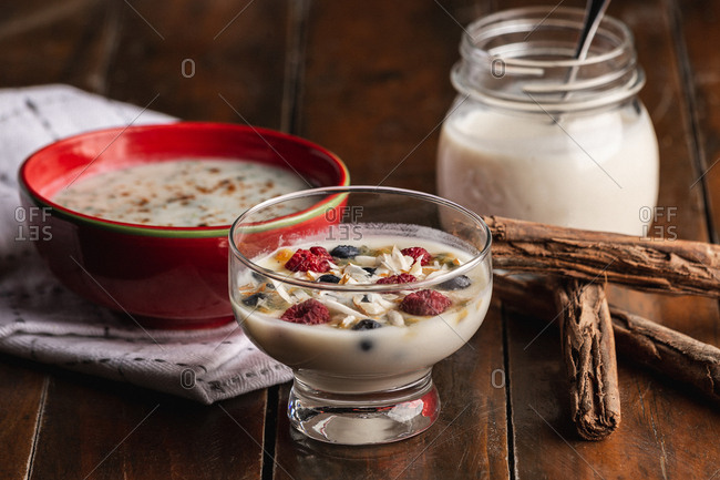 From above appetizing fragrant yogurt with raspberry currant oat in glass and red bowls decorated with cinnamon sticks on wooden background