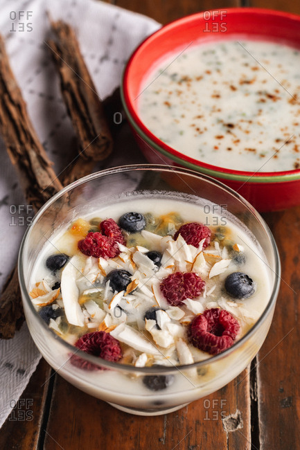 From above appetizing fragrant yogurt with raspberry currant oat in glass and red bowls decorated with cinnamon sticks on wooden background