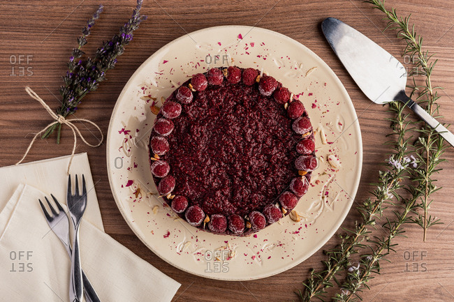 From above juicy fruit cake with raspberries on white plate on wooden background decorated with lavender bouquet