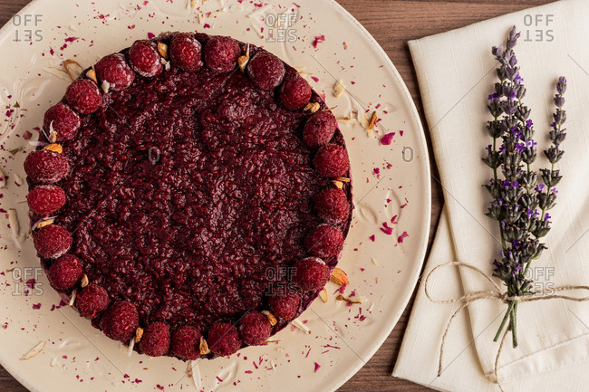 From above juicy fruit cake with raspberries on white plate on wooden background decorated with lavender bouquet