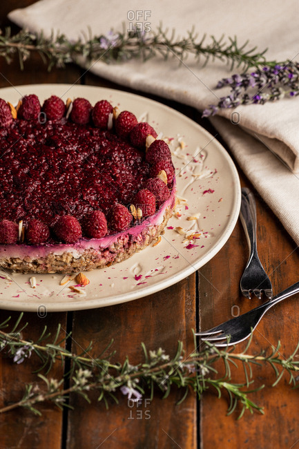 Juicy fruit cake with raspberries on white plate on wooden background decorated with lavender bouquet