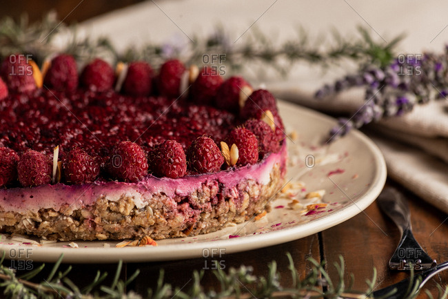 Juicy fruit cake with raspberries on white plate on wooden background decorated with lavender bouquet