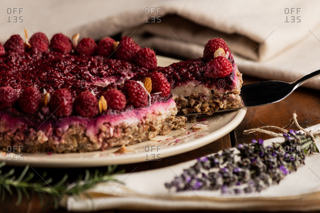 Sliced juicy fruit cake with raspberries on white plate on wooden background decorated with lavender bouquet