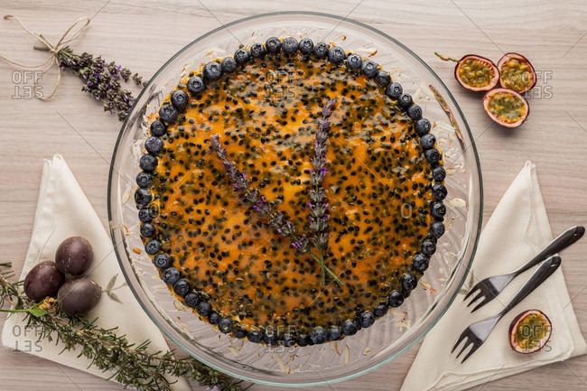 From above appetizing fragrant passion fruit pie with blueberry topping on wooden background decorated with bunch of lavender
