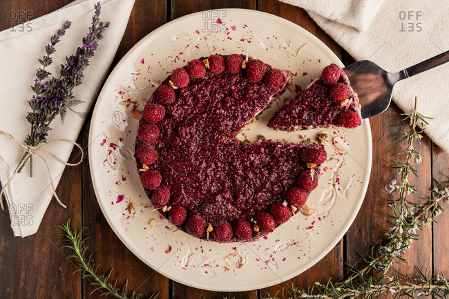 From above sliced juicy fruit cake with raspberries on white plate on wooden background decorated with lavender bouquet