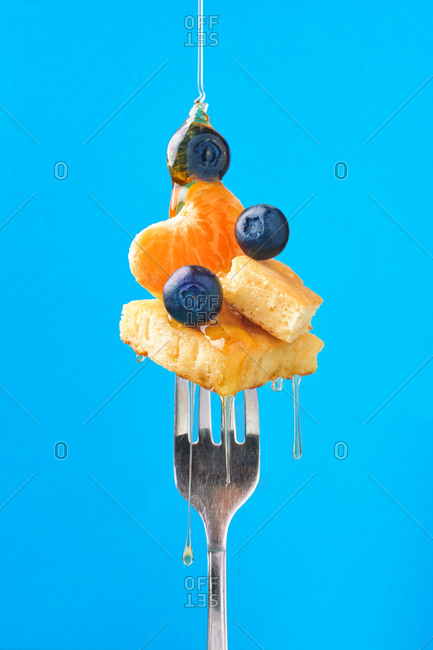 Composition of sweet dessert with strawberry and blueberries flavored by honey on blue background