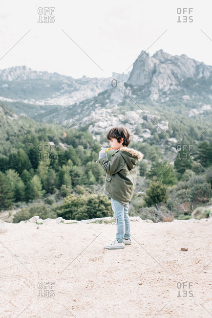 Little curious kid in coat walking down rocky hillside exploring nature