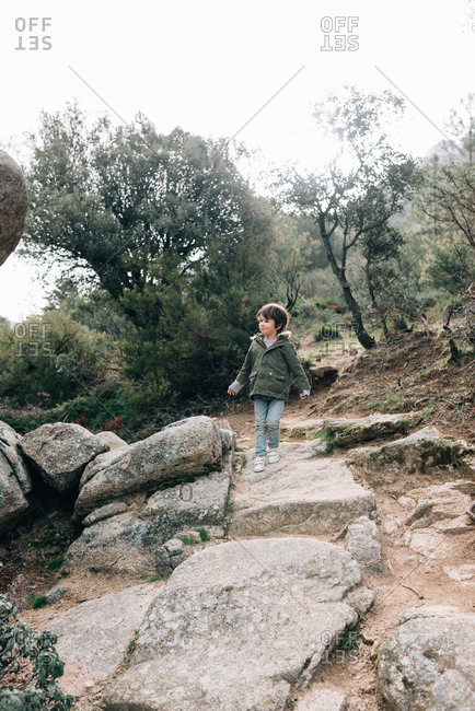 Little curious kid in coat walking down rocky hillside exploring nature