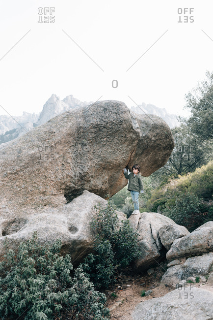 Little curious kid in coat walking down rocky hillside exploring nature