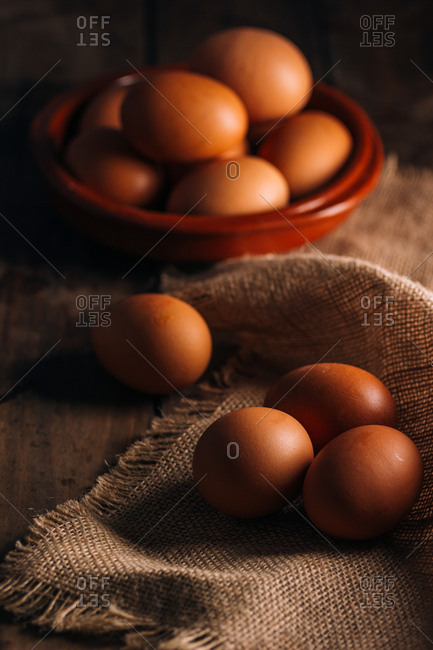 From above brown shiny chickens eggs on linen cloth and in bowl on wooden background