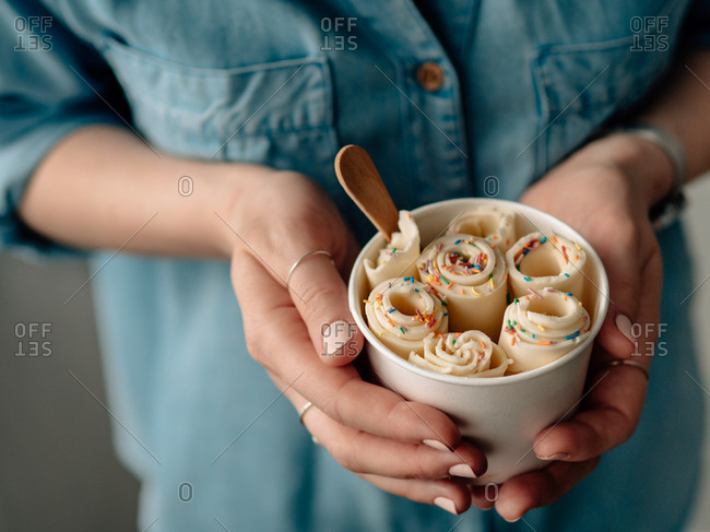 Rolled ice cream in cone cup in woman hands. Woman in jeans shirt holds cone cup with thai style vanilla rolled ice cream