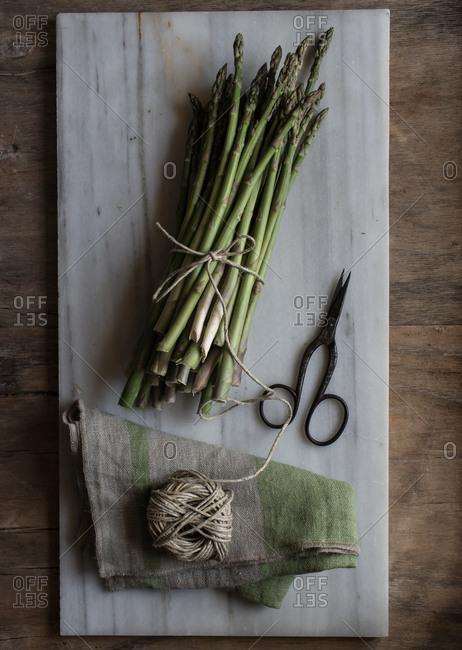 Top view of marble board with pile of asparagus tied with twine rope on wooden table