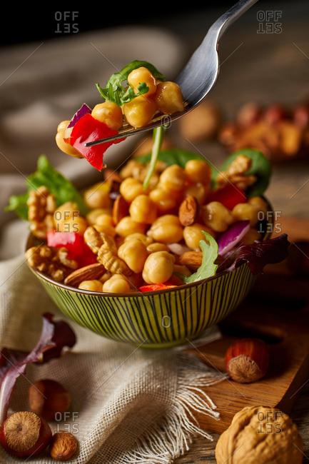 From above appetizing colorful cut vegetable mix with chickpeas and walnuts on wooden background