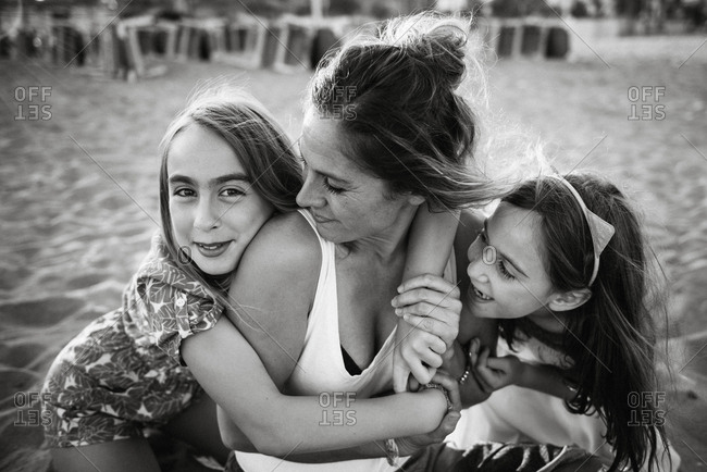 Woman with playful daughters lying on sandy beach having fun together, black and white photo