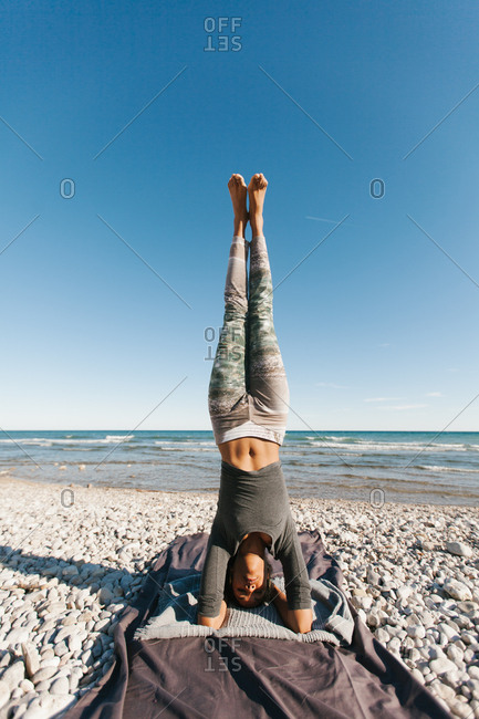 African American attractive young woman in yoga headstand posture in open air on background of calm water in sunny day
