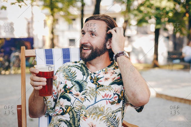 Candid portrait of attractive man in his thirties toasting to his girlfriend with beer on a date on a summer day outdoors.