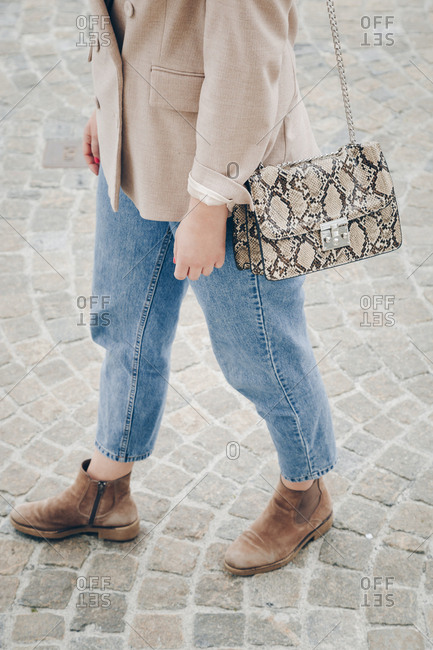 Streetstyle close up of a trendy snake skin purse. Fashionable woman holding a stylish bag in the city, wearing an oversized blazer