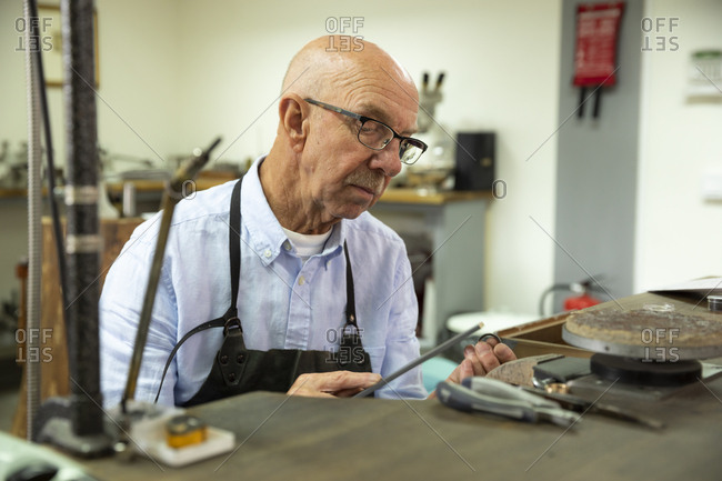 Confident senior male jeweler shaping ring with rasp at workshop