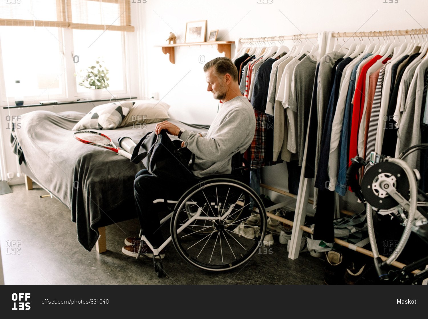Side view of disabled mature man packing tennis racket in bag while sitting on wheelchair at home
