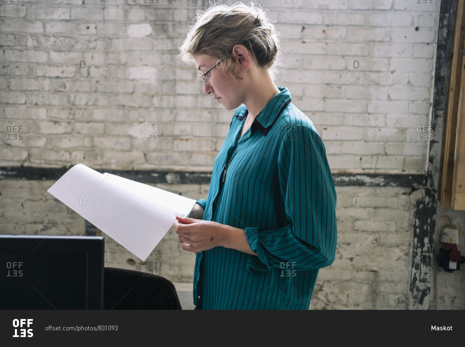Confident young female IT professional reading document standing at creative workplace