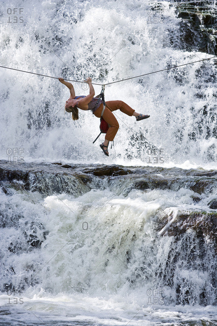 A woman crosses a waterfall using a Tyrolean Traverse on a rope.