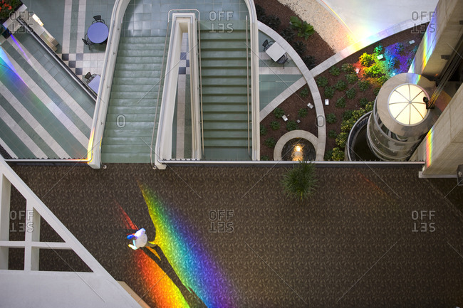 Man walks through a rainbow of spectrum light in a shopping plaza.