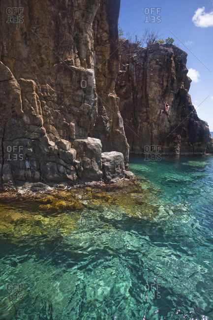 A man climbs a new deep water solo route with clear Caribbean water below.