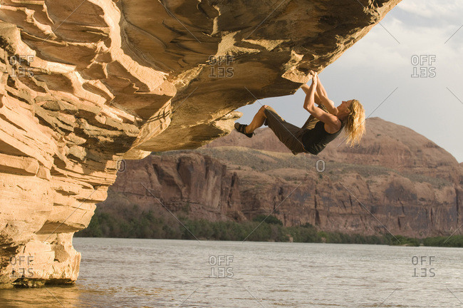 A woman bouldering on an overhanging sandstone rock above the Colorado River outside of Moab, Utah.