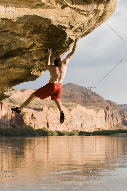 A man bouldering on an overhanging sandstone rock above the Colorado River outside of Moab, Utah.