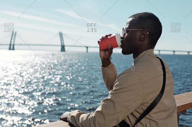 Young man drinking coffee and admiring waterscape