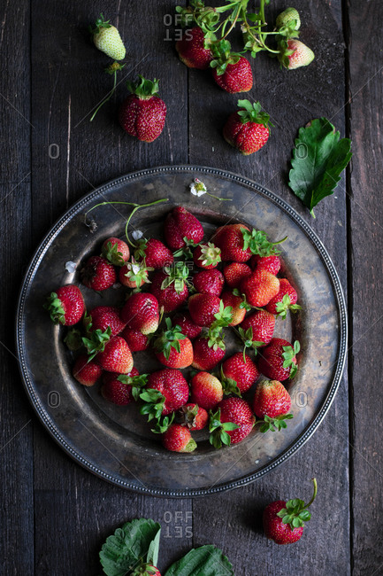 Farm fresh red strawberries, hand-picked and arranged on a rustic plate and placed on a wooden table