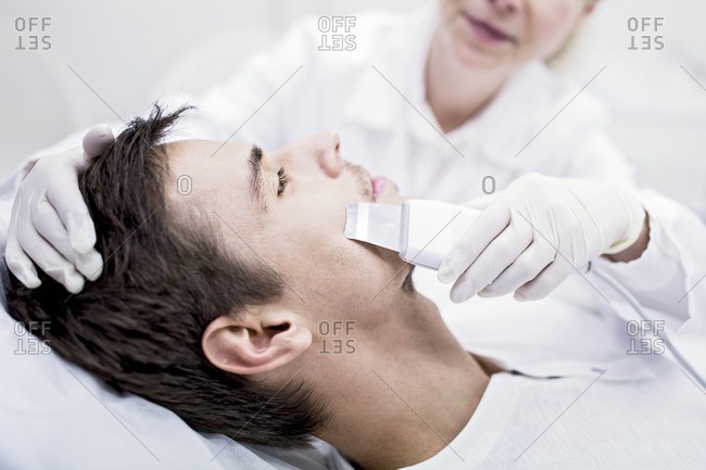 Dermatologist applying facial microdermabrasion treatment on man in clinic, close-up. The cosmetic procedure uses micro crystals to remove dead skin cells. This exfoliating treatment can stimulate the production of collagen and help improve fine lines and acne scarring.