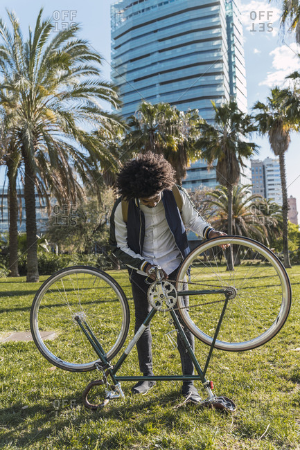 Casual businessman examining bicycle in urban park- Barcelona- Spain