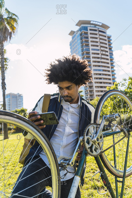 Casual businessman with cell phone and bicycle in urban park- Barcelona- Spain