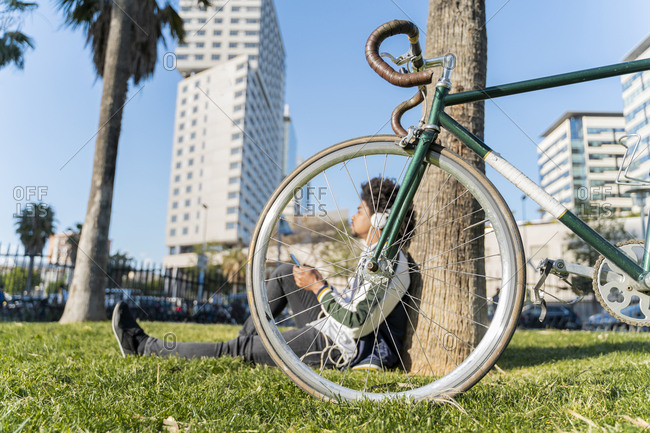 Casual businessman with bicycle taking a break in urban park listening to music- Barcelona- Spain