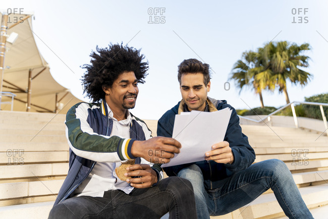 Two casual businessmen sitting on stairs working on paper