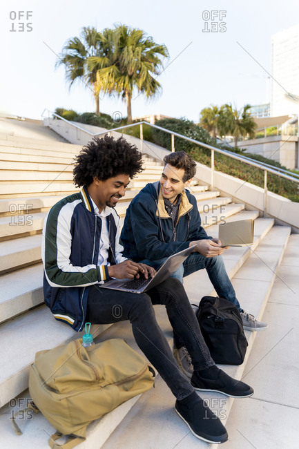 Two casual businessmen sitting on stairs working on laptop