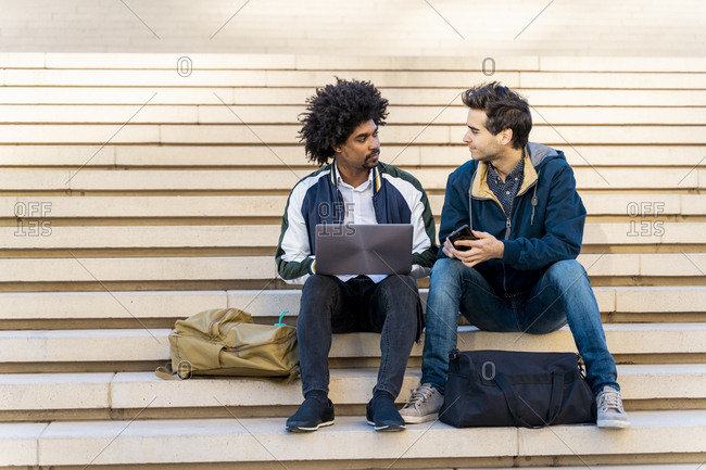 Two casual businessmen sitting on stairs working on laptop