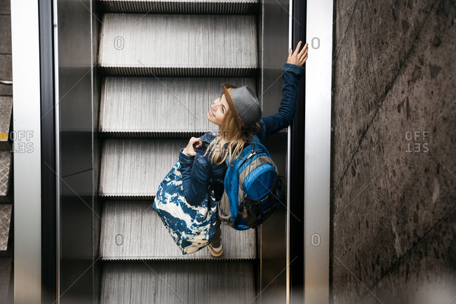 Woman with backpack and travelling bag standing on escalator looking up