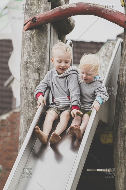 Two barefoot siblings together on a slide