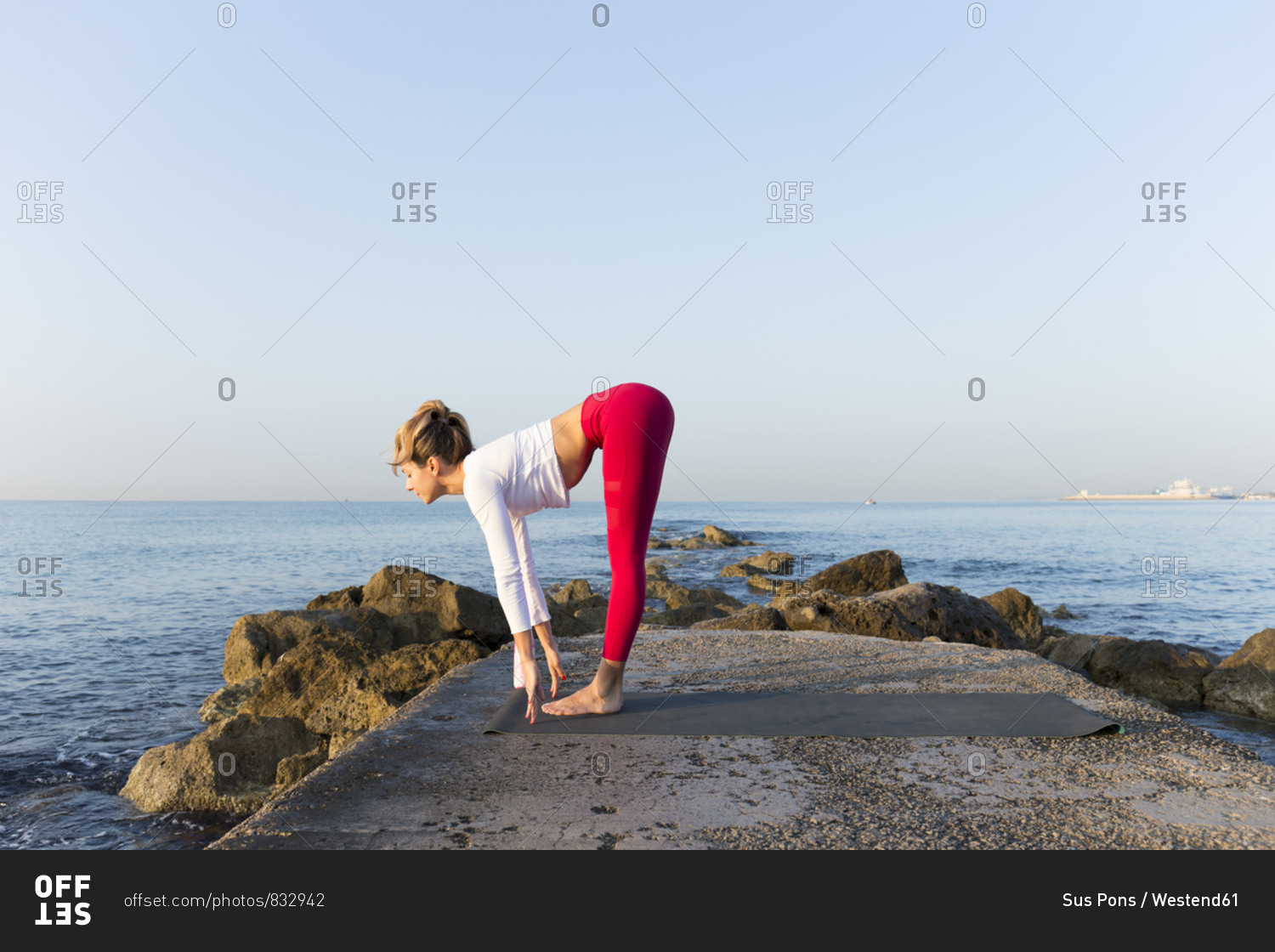 Young woman practicing yoga on the beach- doing sun salutations