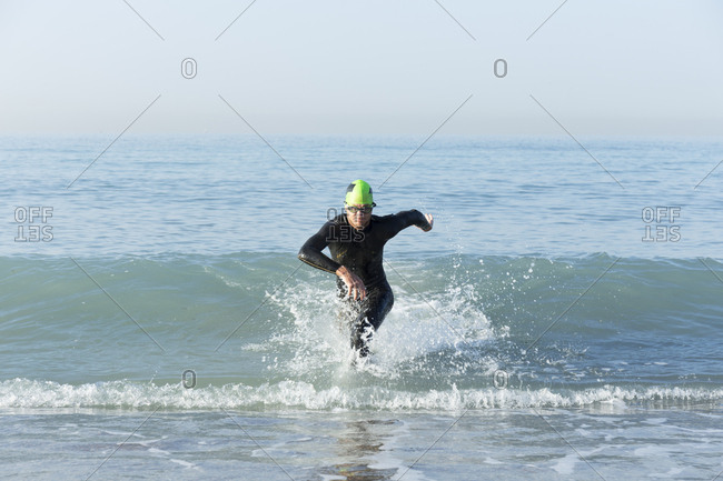 Triathlete in wetsuit running out of the sea