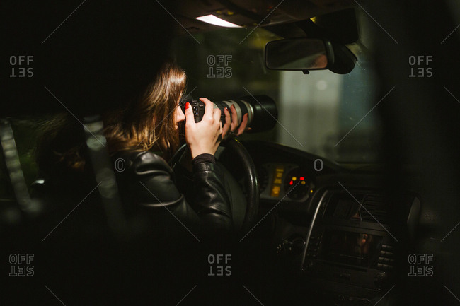 Young woman taking pictures with a camera out of a car at night